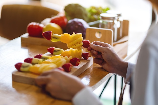 Imagen de primer plano de una hermosa cocinera sosteniendo frutas frescas mezcladas en brochetas en un plato de madera