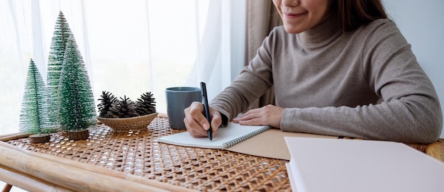 Imagen de primer plano de una hermosa joven asiática escribiendo en un cuaderno mientras estudia en casa