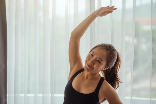 Imagen de primer plano de una hermosa joven asiática estirando sus brazos para calentar antes de entrenar en casa