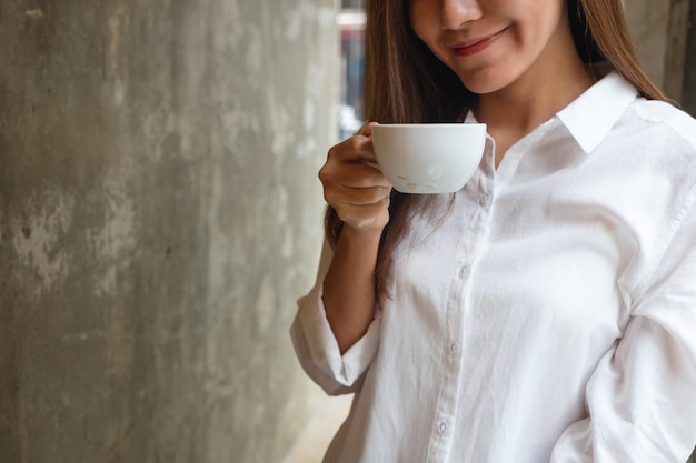 Imagen de primer plano de una hermosa joven asiática oliendo y bebiendo café en la cafetería