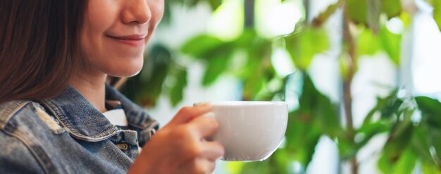 Imagen de primer plano de una hermosa joven asiática sosteniendo y bebiendo café caliente en la cafetería