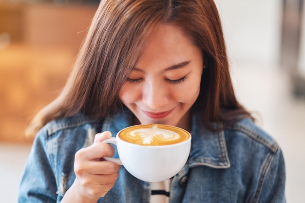 Imagen de primer plano de una hermosa joven asiática sosteniendo y bebiendo café caliente en la cafetería