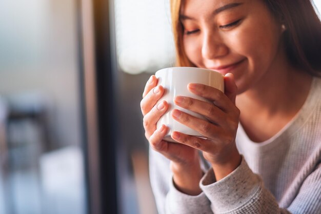 Imagen de primer plano de una hermosa joven asiática sosteniendo y bebiendo café caliente en la cafetería