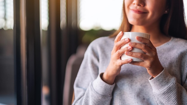 Imagen de primer plano de una hermosa joven asiática sosteniendo y bebiendo café caliente en la cafetería