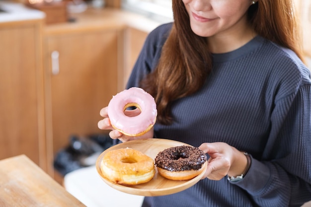 Imagen de primer plano de una hermosa joven asiática sosteniendo y comiendo donas en casa