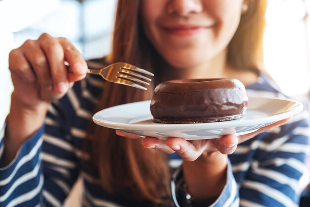 Imagen de primer plano de una hermosa joven asiática sosteniendo y comiendo donas de chocolate