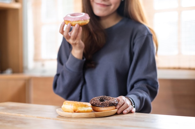 Imagen de primer plano de una hermosa joven asiática sosteniendo y disfrutando comiendo donas en casa