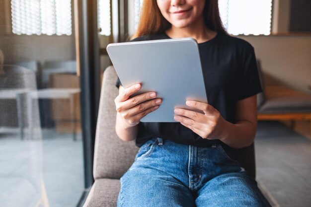 Imagen de primer plano de una hermosa joven asiática sosteniendo y usando una tableta digital en un café