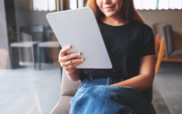 Imagen de primer plano de una hermosa joven asiática sosteniendo y usando una tableta digital en un café