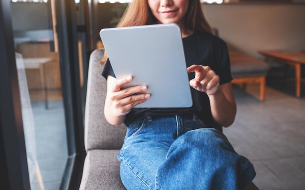 Imagen de primer plano de una hermosa joven asiática sosteniendo y usando una tableta digital en un café