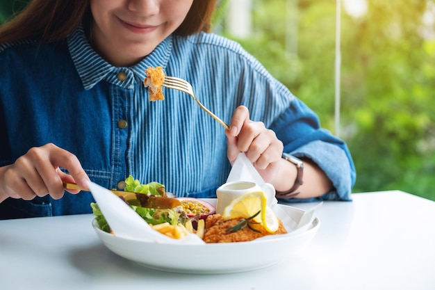 Imagen de primer plano de una hermosa mujer asiática comiendo pescado y papas fritas en la mesa en el restaurante
