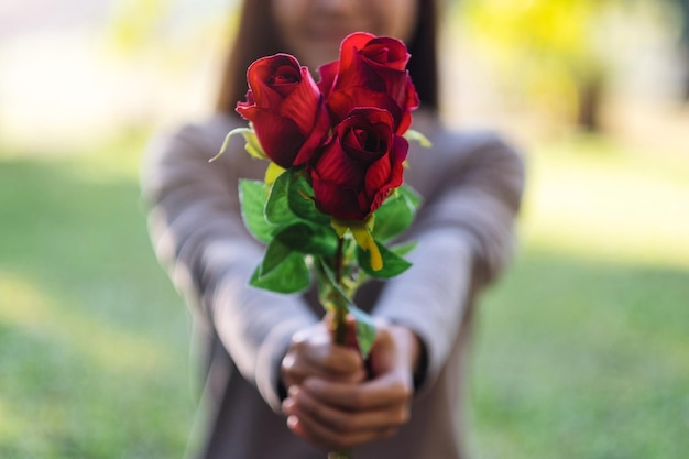 Imagen de primer plano de una hermosa mujer asiática sosteniendo y dando flores de rosas rojas en el parque