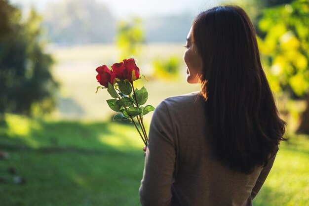 Imagen de primer plano de una hermosa mujer asiática sosteniendo flores de rosas rojas en el parque