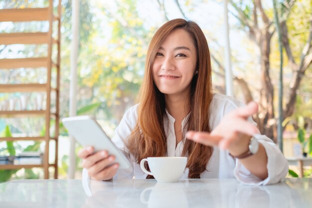 Imagen de primer plano de una hermosa mujer asiática sosteniendo y usando un teléfono móvil en el café