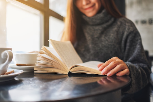 Imagen de primer plano de una hermosa mujer sosteniendo y leyendo un libro con una taza de café sobre la mesa