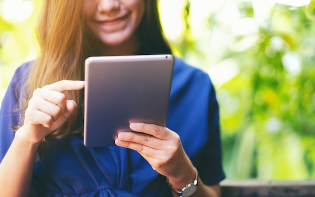 Imagen de primer plano de una hermosa mujer sosteniendo y usando tablet pc mientras está sentado en el jardín