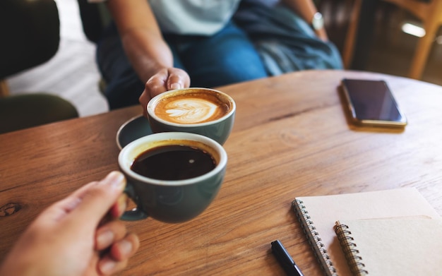 Imagen de primer plano de un hombre y una mujer que tintinean tazas de café con leche en el café