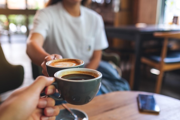 Imagen de primer plano de un hombre y una mujer tintineando tazas de café en la cafetería