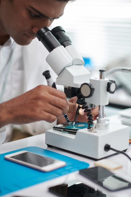 Imagen de primer plano de un ingeniero usando el microscopio al examinar el disco duro