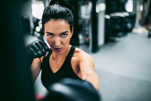 Imagen de primer plano de una joven boxeadora golpeando un enorme saco de boxeo en un estudio de boxeo Sportswoman kickboxer entrenando duro en el gimnasio Estilo de vida deportivo y concepto de personas