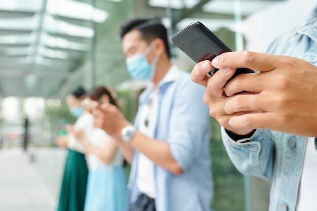 Imagen de primer plano de jóvenes de pie al aire libre con máscaras médicas y enviándose mensajes de texto, se centran en primer plano