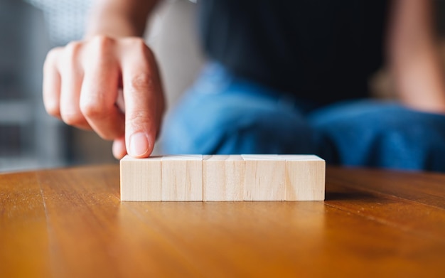 Imagen de primer plano de una mano eligiendo y recogiendo cinco piezas de bloque de cubo de madera en blanco