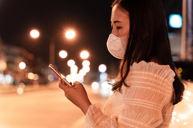 Imagen de primer plano de la mano femenina usando un teléfono inteligente móvil en el concepto de calle de la ciudad de noche de búsqueda o redes sociales