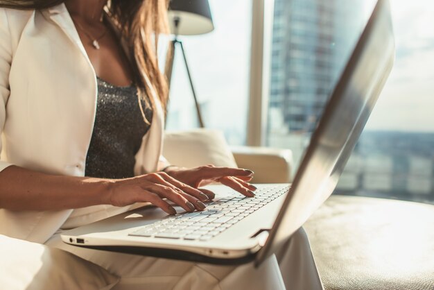 Imagen de primer plano de manos femeninas escribiendo en el teclado de la computadora portátil en la oficina moderna.