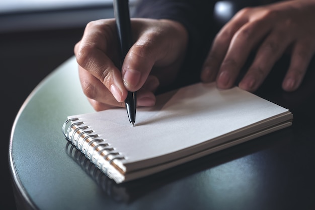 Imagen de primer plano de las manos de una mujer anotando en un cuaderno en blanco blanco en la mesa