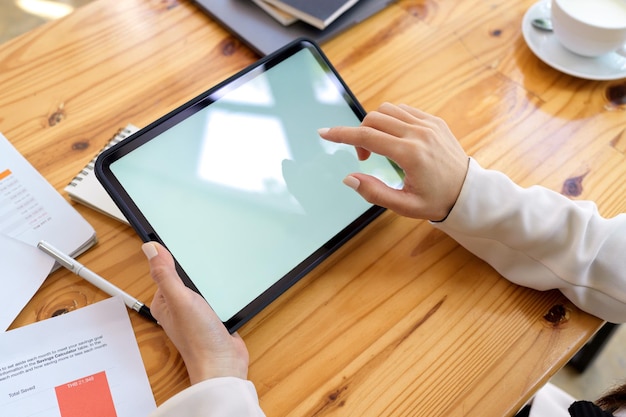 La imagen de primer plano de las manos de una mujer está tocando en la computadora con pantalla táctil de la tableta en el escritorio de trabajo de madera.