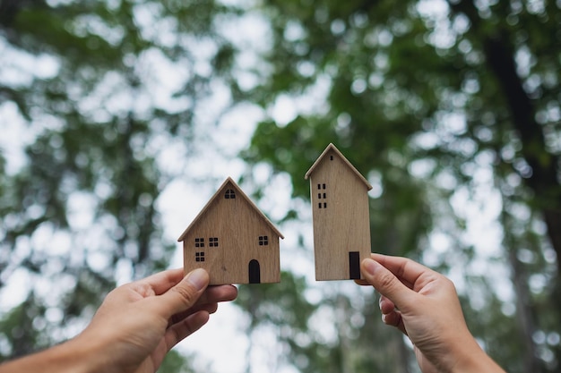 Imagen de primer plano de manos sosteniendo y mostrando modelos de casas de madera con fondo de naturaleza