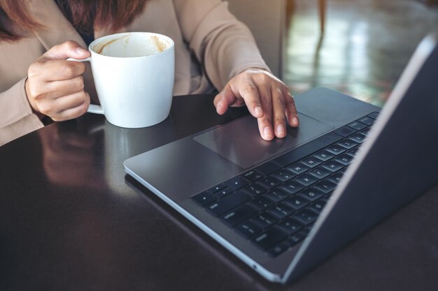 Imagen de primer plano de las manos usando y tocando el panel táctil de la computadora portátil mientras bebe café en la cafetería