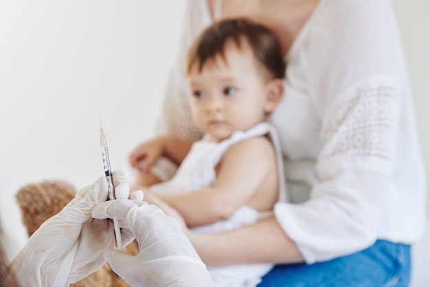 Imagen de primer plano del médico con guantes de goma listo para vacunar a la niña contra la influenza o el coronavirus