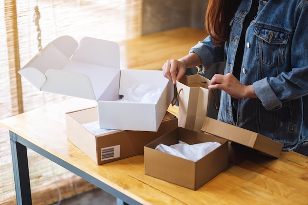 Imagen de primer plano de una mujer abriendo y mirando dentro de la bolsa de compras con caja de paquetería postal sobre la mesa en casa para la entrega y el concepto de compras en línea