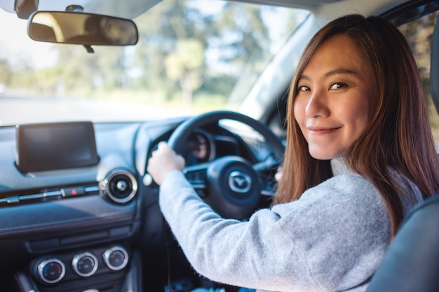 Imagen de primer plano de una mujer asiática sosteniendo el volante mientras conduce un coche