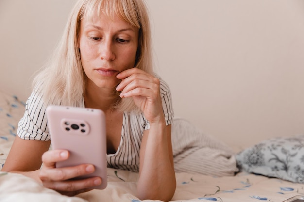 Imagen de primer plano de una mujer bonita acostada en el acogedor interior de la casa y usando un moderno dispositivo de teléfono inteligente manos femeninas escribiendo mensajes de texto a través del concepto de redes sociales de teléfonos celulares