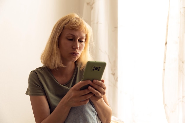 Imagen de primer plano de una mujer bonita sentada en el acogedor interior de la casa y usando un moderno dispositivo de teléfono inteligente manos femeninas escribiendo mensajes de texto a través del concepto de redes sociales de teléfonos celulares