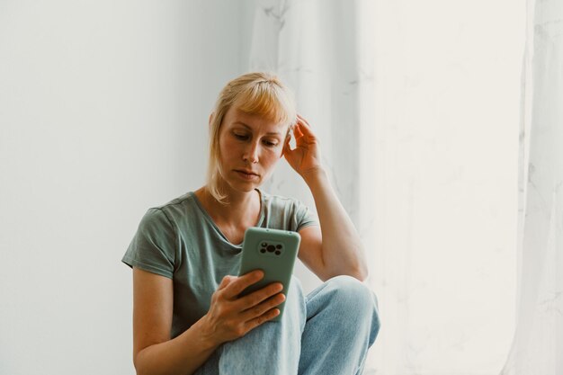 Imagen de primer plano de una mujer bonita sentada en el acogedor interior de la casa y usando un moderno dispositivo de teléfono inteligente manos femeninas escribiendo mensajes de texto a través del concepto de redes sociales de teléfonos celulares