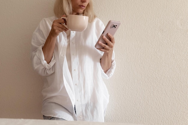 Imagen de primer plano de una mujer bonita sentada en el acogedor interior de la casa y usando un moderno dispositivo de teléfono inteligente manos femeninas escribiendo mensajes de texto a través del concepto de redes sociales de teléfonos celulares