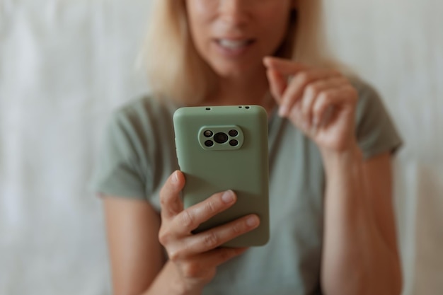 Imagen de primer plano de una mujer bonita sentada en el acogedor interior de la casa y usando un moderno dispositivo de teléfono inteligente manos femeninas escribiendo mensajes de texto a través del concepto de redes sociales de teléfonos celulares