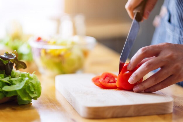 Imagen de primer plano de una mujer chef cortando y picando tomate con un cuchillo en la tabla de madera