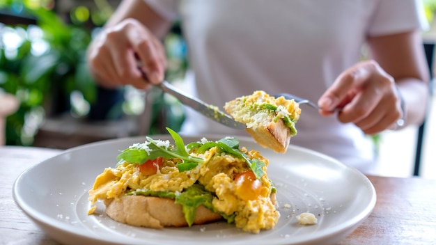 Imagen de primer plano de una mujer comiendo huevos revueltos y sándwich abierto de aguacate