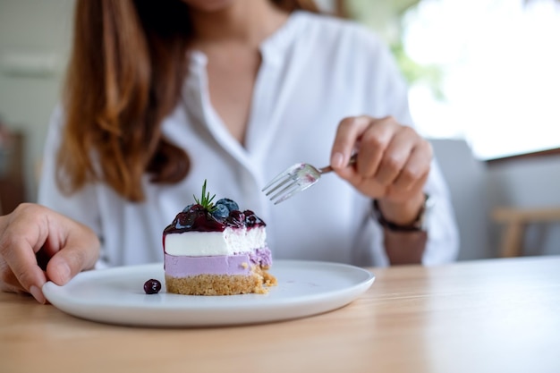 Imagen de primer plano de una mujer comiendo un trozo de tarta de queso con arándanos