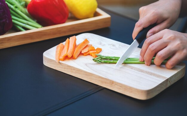 Imagen de primer plano de una mujer cortando y picando espárragos y zanahorias con un cuchillo en una tabla de madera