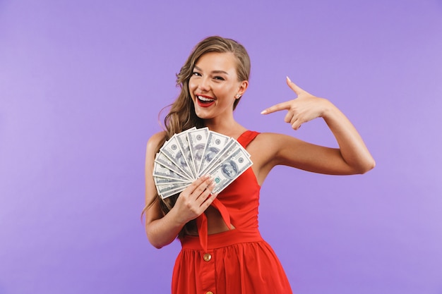 Imagen de primer plano de una mujer encantada con un vestido rojo sonriendo y sosteniendo un abanico de dinero