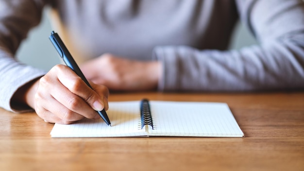 Imagen de primer plano de una mujer escribiendo en un cuaderno en blanco sobre la mesa