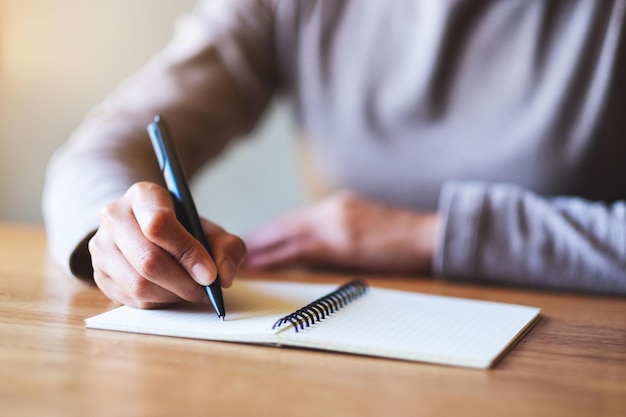 Imagen de primer plano de una mujer escribiendo en un cuaderno en blanco sobre la mesa