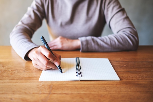 Imagen de primer plano de una mujer escribiendo en un cuaderno en blanco sobre la mesa