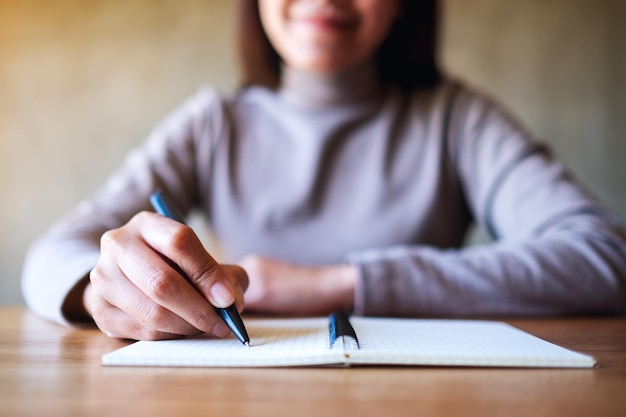 Imagen de primer plano de una mujer escribiendo en un cuaderno en blanco sobre la mesa