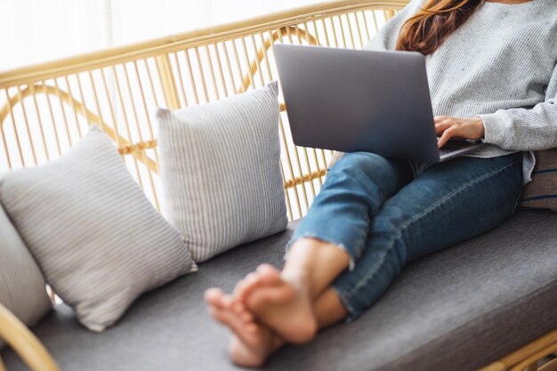 Imagen de primer plano de una mujer joven que usa y trabaja en la computadora portátil mientras está acostado en un sofá en casa